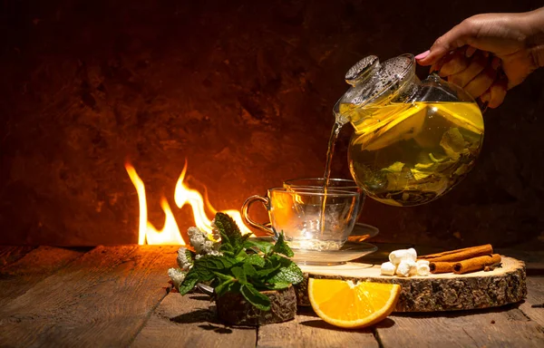 Tea drinking background. Hand pours tea into a cup. Warm atmosphere with fire on a backdrop.