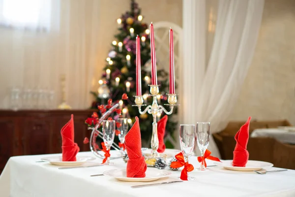 Beautiful holiday table setting for Christmas celebration. Christmas decorated fir tree on a backdrop.