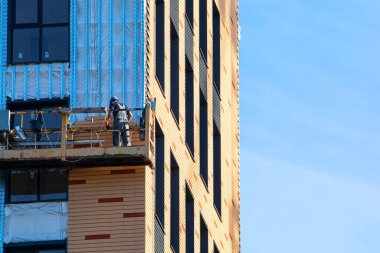 Apartman binası. Yüksek irtifa ve endüstriyel yükseklik. İşçi iskelede durur ve yüzdeki tuğlayı tamir eder..