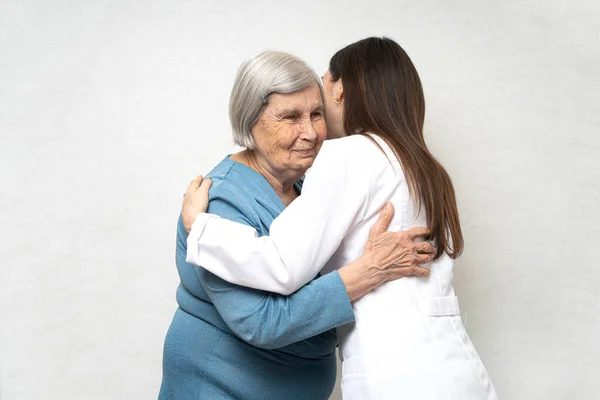 Young doctor hugs an elderly woman. They are happy to see each other and smile. Young doctor takes care for a senior woman.