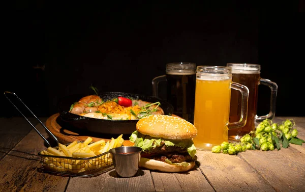 ビールと軽食 テーブルの上にはハンバーガー フライドポテト ソース バヴァリアンソーセージ ビールが並んでいます — ストック写真
