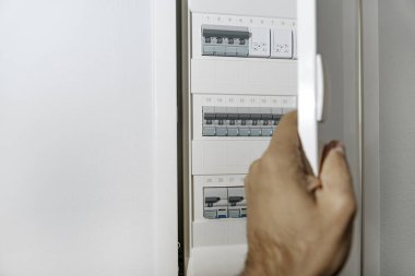 Erkek el, içinde devre kesiciler olan modern elektrik panelini açıyor. Güvenli ev gücü dağıtım sistemi. Kopyalama alanı olan arkaplan.