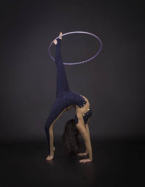 Jimnastik egzersizleri hulahup kız ile sanatsal bir kostümle sirk sanatçısı gerçekleştirir. Karanlık bir arka plan üzerinde çekim stüdyo.