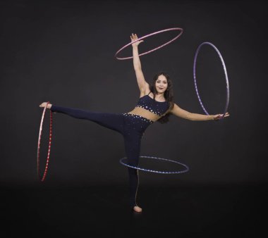 Jimnastik egzersizleri hulahup kız ile sanatsal bir kostümle sirk sanatçısı gerçekleştirir. Karanlık bir arka plan üzerinde çekim stüdyo.