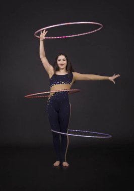 Jimnastik egzersizleri hulahup kız ile sanatsal bir kostümle sirk sanatçısı gerçekleştirir. Karanlık bir arka plan üzerinde çekim stüdyo.