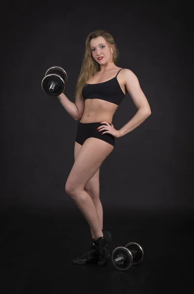 Genç bir kadın fitness dumbbells ile meşgul. Studio siyah arka plan üzerine vurdu. İzole görüntü.