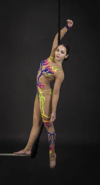 A young girl performs the acrobatic elements in the air trapeze. Studio shooting performances on a black background.