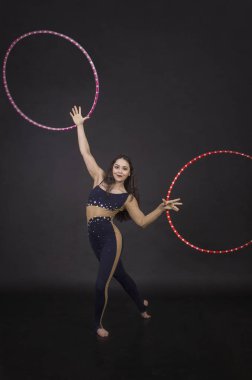 Jimnastik egzersizleri hulahup kız ile sanatsal bir kostümle sirk sanatçısı gerçekleştirir. Karanlık bir arka plan üzerinde çekim stüdyo.