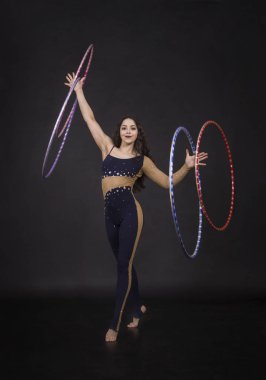 Jimnastik egzersizleri hulahup kız ile sanatsal bir kostümle sirk sanatçısı gerçekleştirir. Karanlık bir arka plan üzerinde çekim stüdyo.