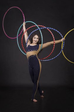 Jimnastik egzersizleri hulahup kız ile sanatsal bir kostümle sirk sanatçısı gerçekleştirir. Karanlık bir arka plan üzerinde çekim stüdyo.