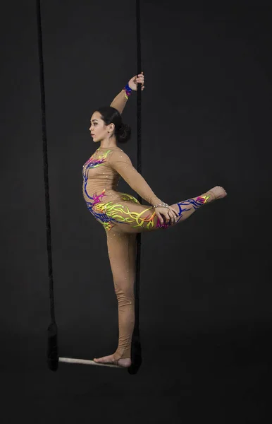 A young girl performs the acrobatic elements in the air trapeze. Studio shooting performances on a black background.