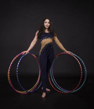 Jimnastik egzersizleri hulahup kız ile sanatsal bir kostümle sirk sanatçısı gerçekleştirir. Karanlık bir arka plan üzerinde çekim stüdyo.