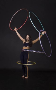 Jimnastik egzersizleri hulahup kız ile sanatsal bir kostümle sirk sanatçısı gerçekleştirir. Karanlık bir arka plan üzerinde çekim stüdyo.