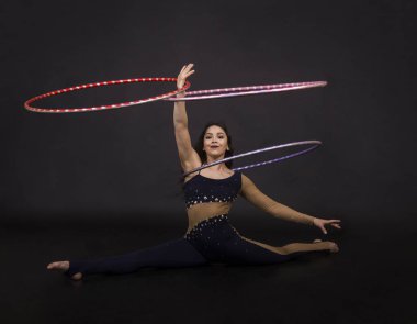 Jimnastik egzersizleri hulahup kız ile sanatsal bir kostümle sirk sanatçısı gerçekleştirir. Karanlık bir arka plan üzerinde çekim stüdyo.