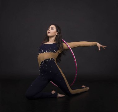 Jimnastik egzersizleri hulahup kız ile sanatsal bir kostümle sirk sanatçısı gerçekleştirir. Karanlık bir arka plan üzerinde çekim stüdyo.