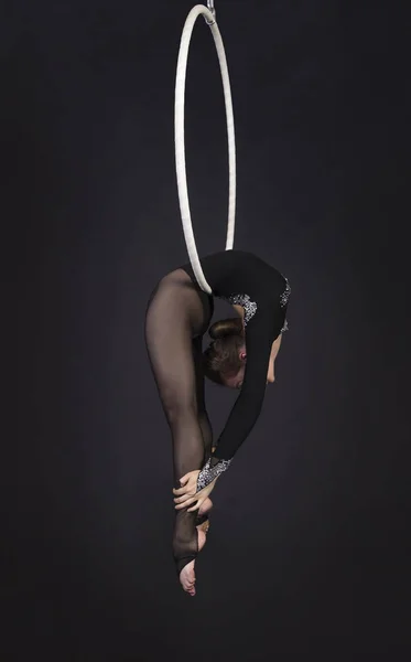 A young girl performs the acrobatic elements in the air ring. Studio shooting performances on a black background.