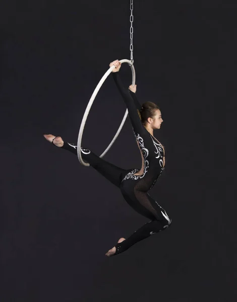 A young girl performs the acrobatic elements in the air ring. Studio shooting performances on a black background.