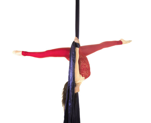 A young girl with long hair in a red suit performs gymnastic and circus exercises on silk. Studio shooting on white background, isolated image.