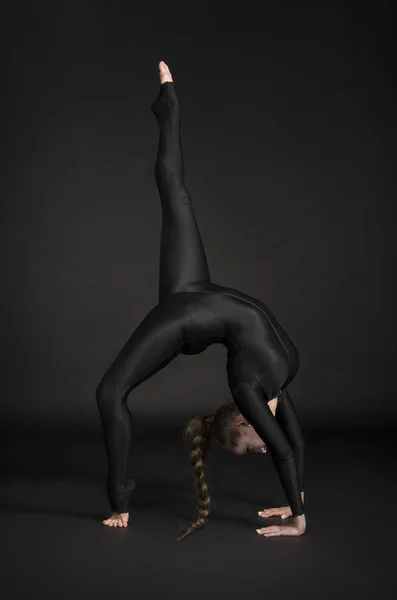 長い髪と黒のスーツの女の子は 体操を実行します 暗い背景で撮影スタジオ — ストック写真