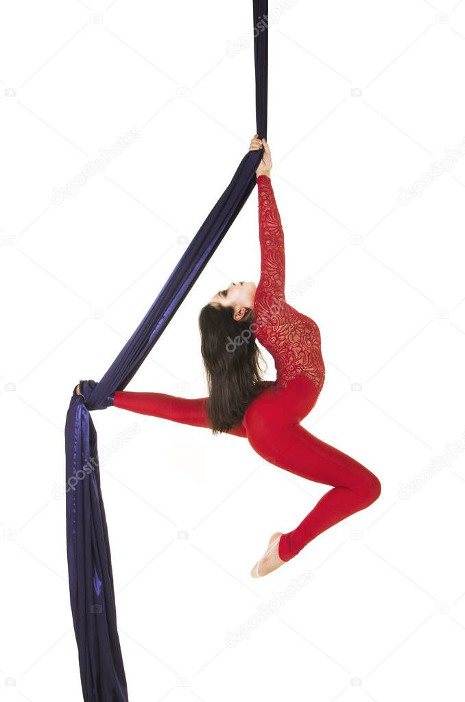 A young girl with long hair in a red suit performs gymnastic and circus exercises on silk. Studio shooting on white background, isolated image.