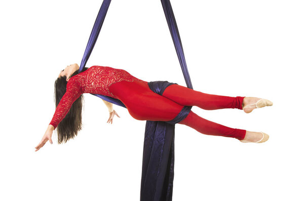 A young girl with long hair in a red suit performs gymnastic and circus exercises on silk.