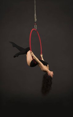 Koyu renk takım elbiseli ve tozluklu bir kız hava halkasında akrobatik elementler icra ediyor..