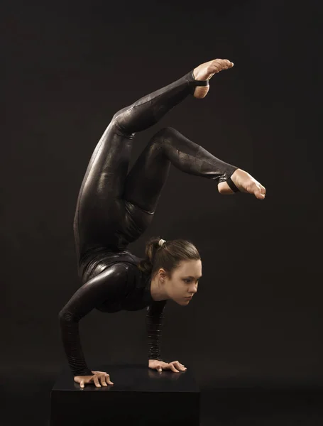 Una ragazza affascinante ginnasta, in abito nero, impegnata in acrobazie alla luce della contra . — Foto Stock