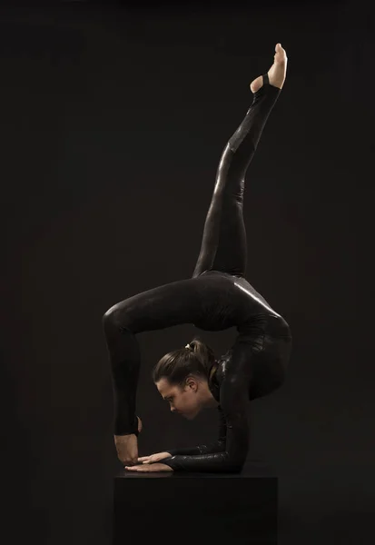 Очаровательная девушка гимнастка, в черном костюме, занимается акробатикой в свете контрас . — стоковое фото