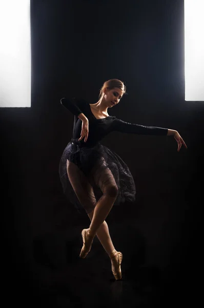 Okouzlující dívka baletka v černém obleku tančí balet ve světle rozvrhu . — Stock fotografie