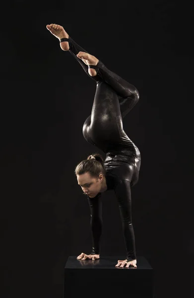 Una chica encantadora gimnasta, en un traje negro, dedicada a las acrobacias a la luz de la contra . — Foto de Stock