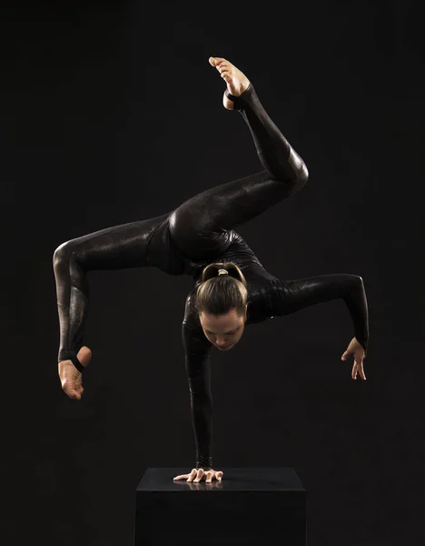 Okouzlující dívčí gymnastka v černém obleku, která se zabývá akrobacií ve světle kontra. — Stock fotografie