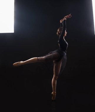 Siyah takım elbiseli sevimli kız balerin, kontur ışığında bir bale dans ediyor .