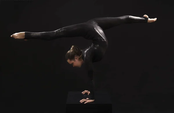 一个迷人的女孩体操运动员，在黑色西装，从事杂技的光的对比. — 图库照片
