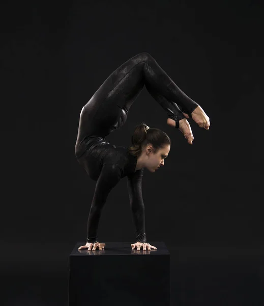 一个迷人的女孩体操运动员，在黑色西装，从事杂技的光的对比. — 图库照片