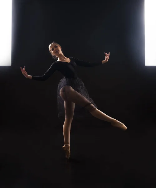Charming girl ballerina in a black suit, is dancing a ballet in the light of the contour . Shooting a performance on a dark background.