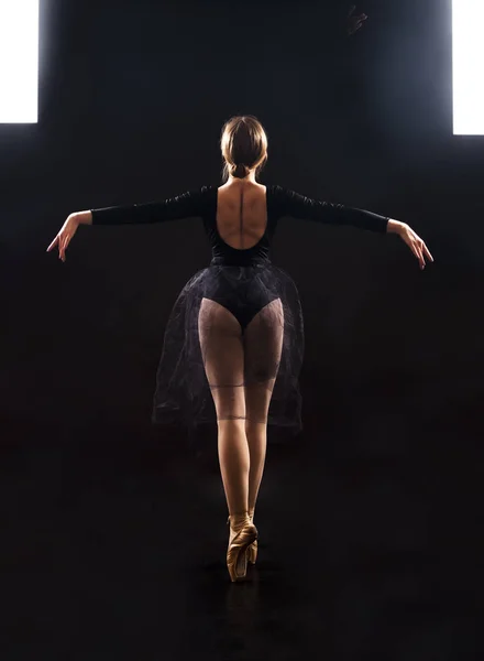 Charming girl ballerina in a black suit, is dancing a ballet in the light of the contour . Shooting a performance on a dark background.