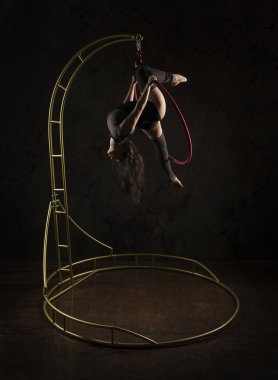 Muhteşem kız, hava akrobat, koyu bir takım elbise içinde sahne ışığında, taşınabilir bir hava halkası üzerinde akrobatik elemanları gerçekleştirir.