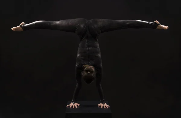 Очаровательная девушка гимнастка, в черном костюме, занимается акробатикой в свете контрас . — стоковое фото