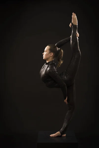 Okouzlující dívčí gymnastka v černém obleku, která se zabývá akrobacií ve světle kontra. — Stock fotografie