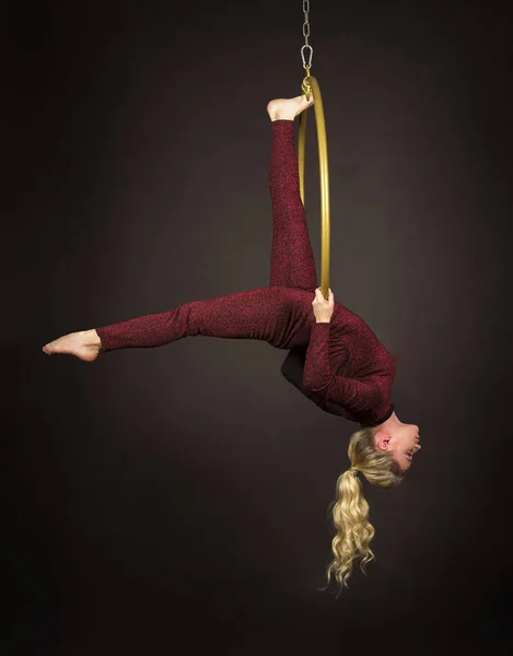 A slender blonde girl-an air acrobat in a red suit with long hair , performs exercises in an air ring.