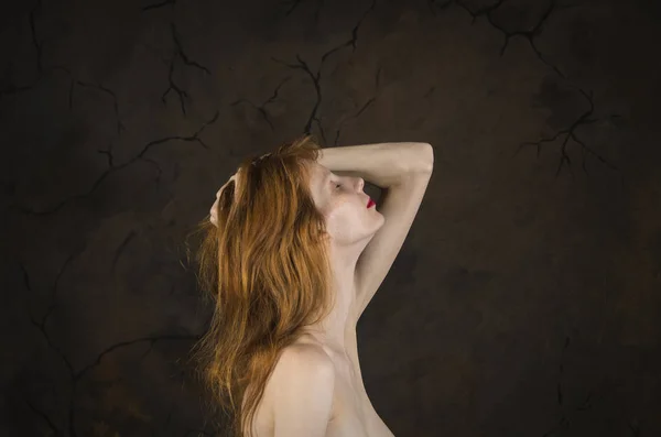 Portrait of a thin girl with bare shoulders, long,red hair and freckles on a dark background.