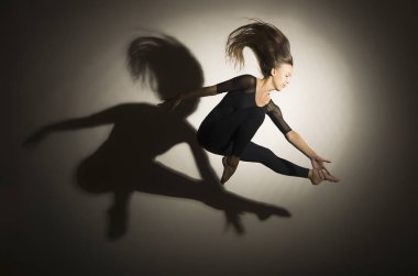 Karanlıkta kız jimnastik atlama gerçekleştirir, beyaz bir arka plan üzerinde bir şekil bir gölge var.