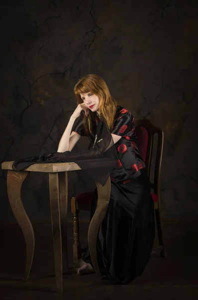 Chica pelirroja con ropa oscura sentada a la mesa . — Foto de Stock