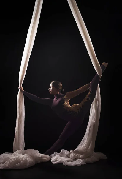 Спортивний дівчина в бордовому костюмі виконує гімнастичні і циркові вправи на білому шовку, в протипоказання світла. — стокове фото