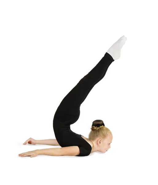 En liten flicka i svart gymnastik kostym utför gymnastiska övningar på en vit bakgrund. — Stockfoto