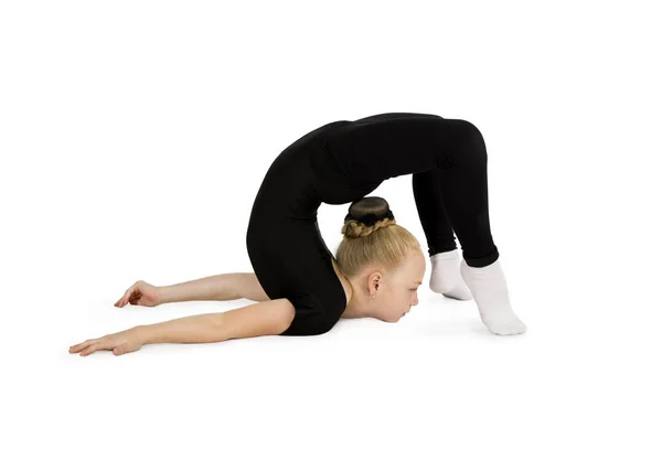 Malá dívka v černém gymnastickém obleku provádí gymnastická cvičení na bílém pozadí. — Stock fotografie
