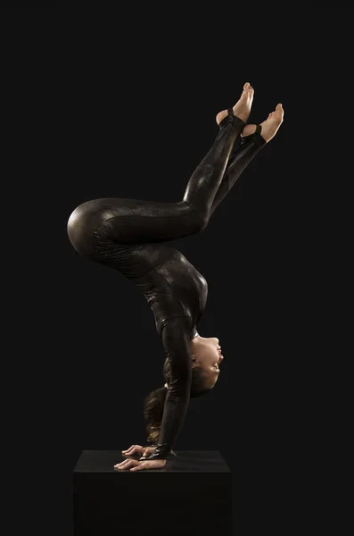 A charming girl gymnast, in a black suit, engaged in acrobatics in the light of the contra. — Stock Photo, Image