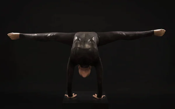 Une charmante fille gymnaste, en costume noir, engagée dans des acrobaties à la lumière de la contra . — Photo