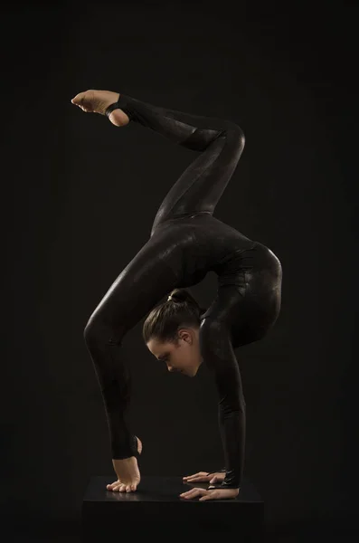 A charming girl gymnast, in a black suit, engaged in acrobatics in the light of the contra. — Stock Photo, Image