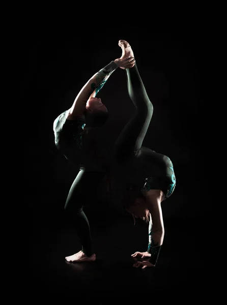 Due giovani equilibristi femminili eseguono elementi acrobatici su sfondo scuro in illuminazione sagomata. — Foto Stock